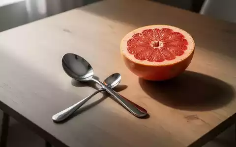 Ein polierter Grapefruitlöffel liegt neben einer halbierten Grapefruit auf einem minimalistischen Holztisch. - Foto: über boerse-global.de