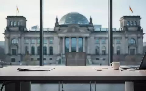 Ein minimalistischer Schreibtisch vor dem unscharfen Reichstagsgebäude als Symbol für sozialpolitische Reformen. - Foto: über boerse-global.de