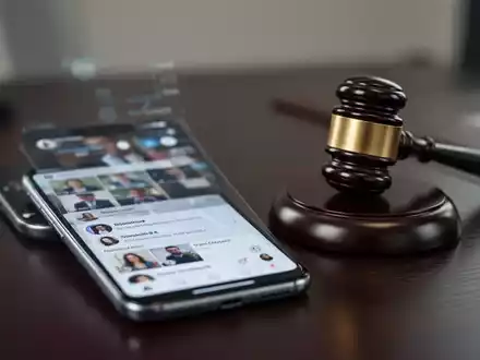 Ein Smartphone mit Social-Media-Profil neben einem Richterhammer auf einem Schreibtisch als Symbol für rechtliche Folgen. - Foto: über boerse-global.de