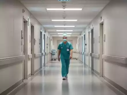 Ein medizinischer Mitarbeiter in einem modernen Krankenhausflur steht symbolisch für die Herausforderungen der Pflege. - Foto: über boerse-global.de