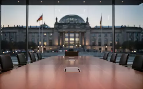 Ein moderner Konferenztisch vor dem unscharfen Reichstagsgebäude, symbolisch für politische Verhandlungen. - Foto: über boerse-global.de