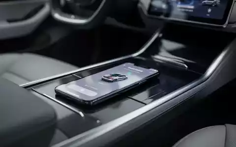 Ein Smartphone mit digitalem Autoschlüssel-Interface liegt auf der Mittelkonsole eines modernen Elektrofahrzeugs. - Foto: über boerse-global.de