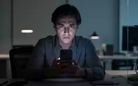 Eine Person hält nachdenklich ein Smartphone in einer modern beleuchteten Arbeitsumgebung. - Foto: über boerse-global.de
