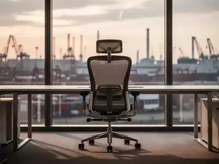 Ein leerer Büroarbeitsplatz mit einem ergonomischen Stuhl vor einem Fenster mit Blick auf ein urbanes Industriegebiet. - Foto: über boerse-global.de