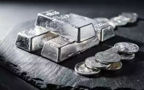 Silberbarren und glänzende Silbermünzen auf einer dunklen Oberfläche bei dramatischem Licht. - Foto: über boerse-global.de