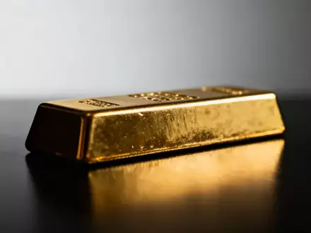 Ein einzelner Goldbarren auf einer dunklen, reflektierenden Oberfläche bei gedimmter Beleuchtung. - Foto: über boerse-global.de