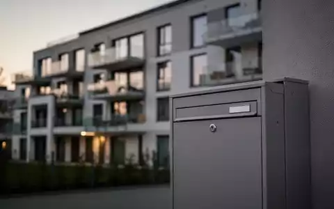 Ein modernes Wohngebäude mit Briefkasten im Vordergrund als Symbol für die Wohngeldreform und staatliche Einsparungen. - Foto: über boerse-global.de