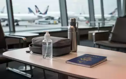 Reise-Set mit Handdesinfektion und Wasserflasche auf einem Tisch in einem modernen Flughafen-Terminal. - Foto: über boerse-global.de