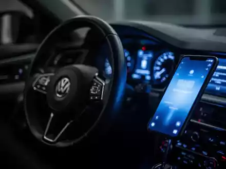 Ein verschwommenes Autocockpit, in dem das Display eines Smartphones den Innenraum in kaltes blaues Licht taucht. - Foto: über boerse-global.de