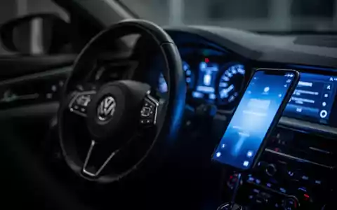Ein verschwommenes Autocockpit, in dem das Display eines Smartphones den Innenraum in kaltes blaues Licht taucht. - Foto: über boerse-global.de