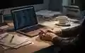 Ein unaufgeräumter Schreibtisch im Homeoffice mit Laptop und Kaffeetasse bei gedimmtem, stimmungsvollem Licht. - Foto: über boerse-global.de