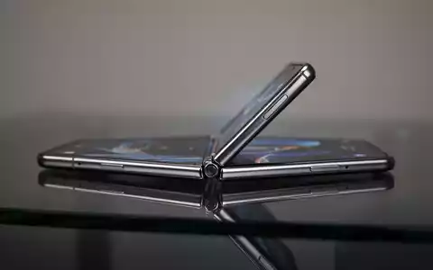 Ein schlankes, metallisches Falt-Smartphone, teilweise geöffnet auf dunkler Fläche, um das Scharnier-Design hervorzuheben. - Foto: über boerse-global.de