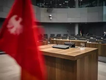 Ein verschwommenes rotes Parteisymbol vor einer parlamentarischen Kulisse, das eine angespannte politische Stimmung vermittelt. - Foto: über boerse-global.de