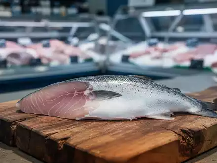 Frisches Fischfilet auf einem Holzbrett vor einem verschwommenen Hintergrund einer Fischtheke im Supermarkt. - Foto: über boerse-global.de