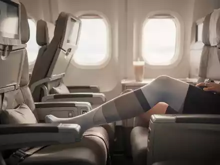 Passagier im Flugzeug trägt Kompressionsstrümpfe zur Vorbeugung von Thrombosen während eines Langstreckenflugs. - Foto: über boerse-global.de