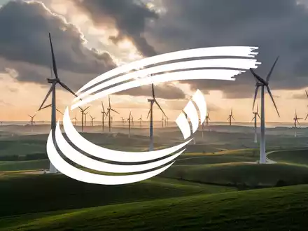 Moderne Windkraftanlagen in einer grünen Hügellandschaft bei Sonnenuntergang. - Foto: über boerse-global.de