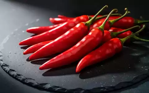 Frische rote Chilischoten auf einem dunklen Steinhintergrund in einer professionellen, kontrastreichen Nahaufnahme. - Foto: über boerse-global.de