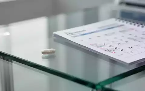 Eine einzelne Tablette liegt neben einem Kalenderblatt und symbolisiert den wöchentlichen Einnahmerhythmus bei HIV-Therapien. - Foto: über boerse-global.de