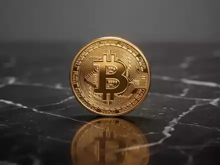 Eine einzelne Bitcoin-Münze auf einer glänzenden dunklen Oberfläche bei neutraler Beleuchtung. - Foto: über boerse-global.de