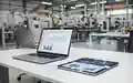 Modernes Büro-Setup mit Laptop und Tablet vor verschwommenem Hintergrund einer Industrieanlage. - Foto: über boerse-global.de