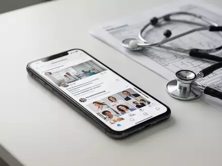 Ein Smartphone mit sozialen Medien auf einem Schreibtisch neben einem Stethoskop und medizinischen Unterlagen. - Foto: über boerse-global.de