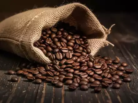 Kaffeebohnen, die aus einem Jutesack auf einen dunklen Holztisch geschĂŒttet werden. - Foto: ĂŒber boerse-global.de