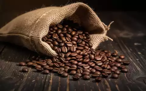 Kaffeebohnen, die aus einem Jutesack auf einen dunklen Holztisch geschüttet werden. - Foto: über boerse-global.de