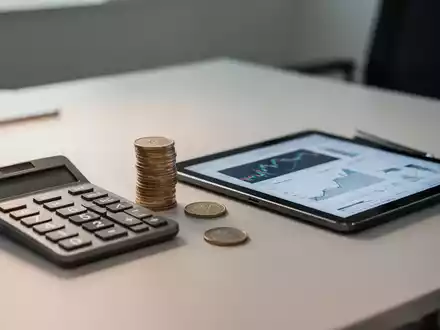 Ein Schreibtisch mit einem Taschenrechner und Euromünzen, die die finanzielle Situation und Zuverdienstmöglichkeiten symbolisieren. - Foto: über boerse-global.de