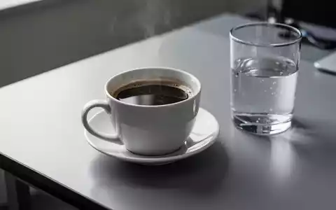Eine Tasse schwarzer Kaffee neben einem Glas Wasser auf einem modernen Schreibtisch. - Foto: über boerse-global.de