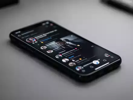 Ein Smartphone zeigt eine Social-Media-App auf einem Schreibtisch bei gedimmtem Licht. - Foto: über boerse-global.de