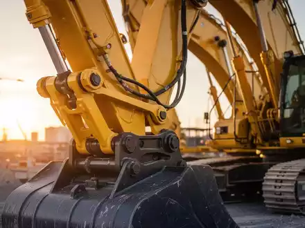 Moderner Hydraulikbagger auf einer Baustelle bei Sonnenuntergang, Fokus auf mechanische Bauteile und Stahlkonstruktion. - Foto: über boerse-global.de