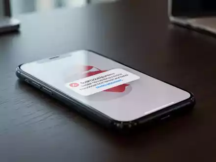Ein Smartphone auf einem Schreibtisch zeigt eine verdächtige Benachrichtigung, die auf einen SMS-Betrug hindeutet. - Foto: über boerse-global.de