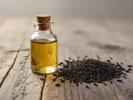 Eine kleine Glasflasche mit goldenem Schwarzkümmelöl neben verstreuten Schwarzkümmelsamen auf einem rustikalen Holztisch. - Foto: über boerse-global.de