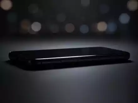 Schlankes, minimalistisches Smartphone-Silhouette auf dunkler, reflektierender Fläche mit filmischer Beleuchtung. - Foto: über boerse-global.de