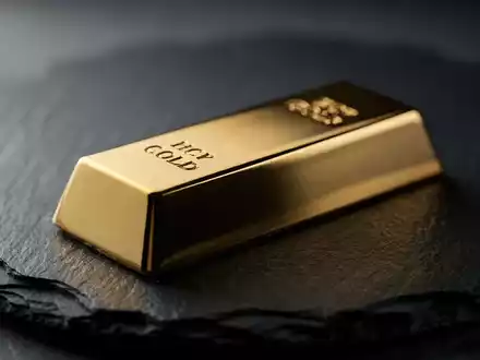 Ein glänzender Goldbarren auf einer dunklen Schieferplatte bei stimmungsvoller Beleuchtung. - Foto: über boerse-global.de