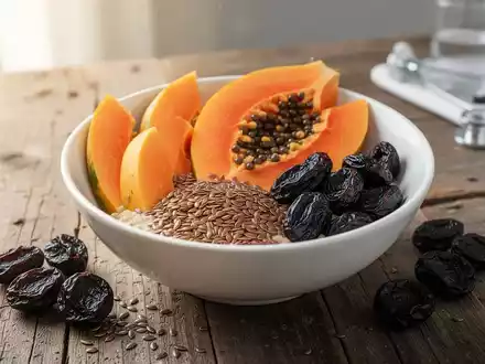 Eine Auswahl gesunder Lebensmittel wie Papaya, Leinsamen und Trockenpflaumen auf einem Holztisch zur Darmgesundheit. - Foto: über boerse-global.de