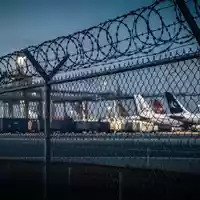 Sicherheitszaun mit Stacheldraht vor einem Frachtflughafen bei Dämmerung. - Foto: über boerse-global.de