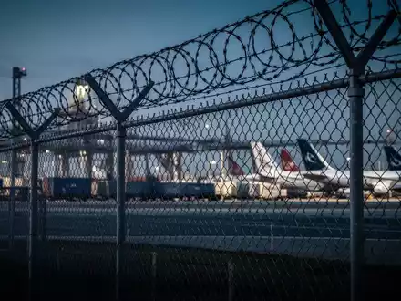 Sicherheitszaun mit Stacheldraht vor einem Frachtflughafen bei Dämmerung. - Foto: über boerse-global.de