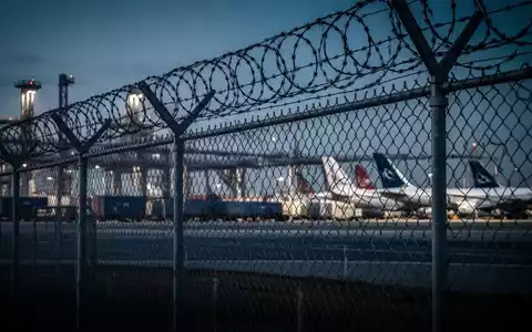 Sicherheitszaun mit Stacheldraht vor einem Frachtflughafen bei Dämmerung. - Foto: über boerse-global.de