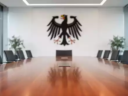 Modernes Büro im Bundeskanzleramt mit einem Konferenztisch vor einem unscharfen Hintergrund eines Staatswappens. - Foto: über boerse-global.de