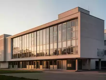 Die ikonische Glasfassade des Bauhausgebäudes in Dessau bei klarem Licht, die die minimalistische Architektur betont. - Foto: über boerse-global.de