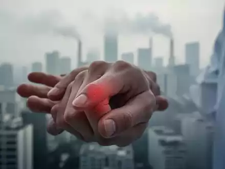 Nahaufnahme einer Hand mit Gelenkentzündung vor einem verschwommenen, dunstigen Stadtbild als Symbol für Luftverschmutzung. - Foto: über boerse-global.de