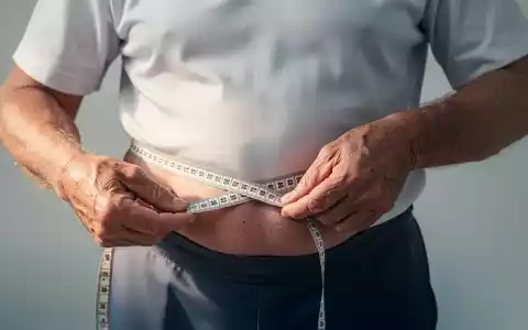 Eine Person über 50 Jahre misst ihren Taillenumfang mit einem Maßband, symbolisch für das Gesundheitsrisiko durch Bauchfett. - Foto: über boerse-global.de