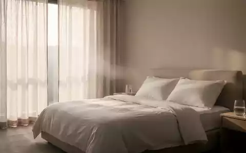 Ein minimalistisch eingerichtetes, kühles Schlafzimmer mit leichter Bettwäsche und zugezogenen Vorhängen an einem Sommertag. - Foto: über boerse-global.de