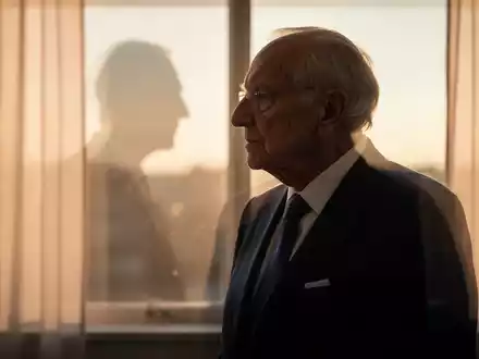 Nachdenkliche Silhouette eines älteren Mannes in einem formellen Anzug vor einem Fenster bei goldenem Licht. - Foto: über boerse-global.de