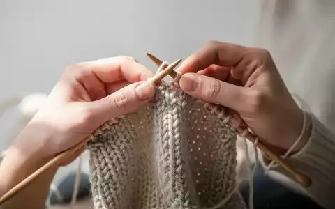 Nahaufnahme von Händen beim Stricken als bewusste Methode zur Entschleunigung und Burnout-Prävention. - Foto: über boerse-global.de