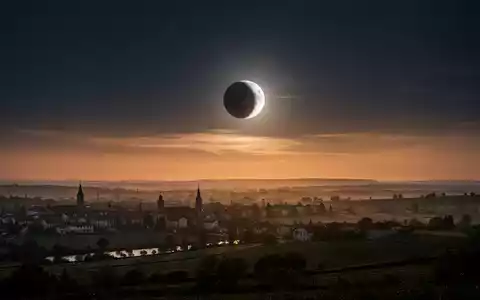 Eine partielle Sonnenfinsternis am Abendhimmel über einer ruhigen Landschaft während des Sonnenuntergangs. - Foto: über boerse-global.de