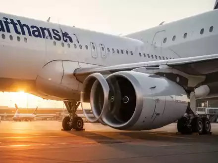 Ein Lufthansa-Passagierflugzeug steht bei goldenem Licht auf dem Rollfeld eines Flughafens. - Foto: über boerse-global.de