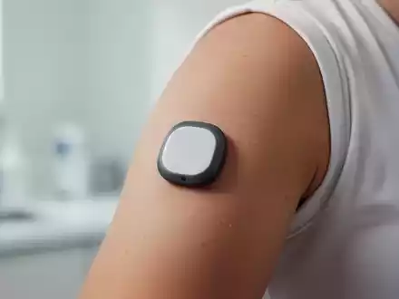 Ein am Oberarm befestigter Glukose-Sensor zur kontinuierlichen Messung vor einem unscharfen Hintergrund. - Foto: über boerse-global.de