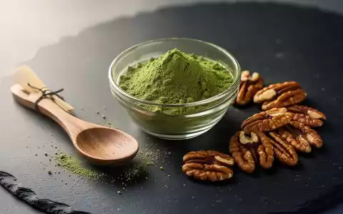 Eine Schale mit Matcha-Pulver, ein Holzlöffel und Pekannüsse auf einem dunklen Untergrund. - Foto: über boerse-global.de